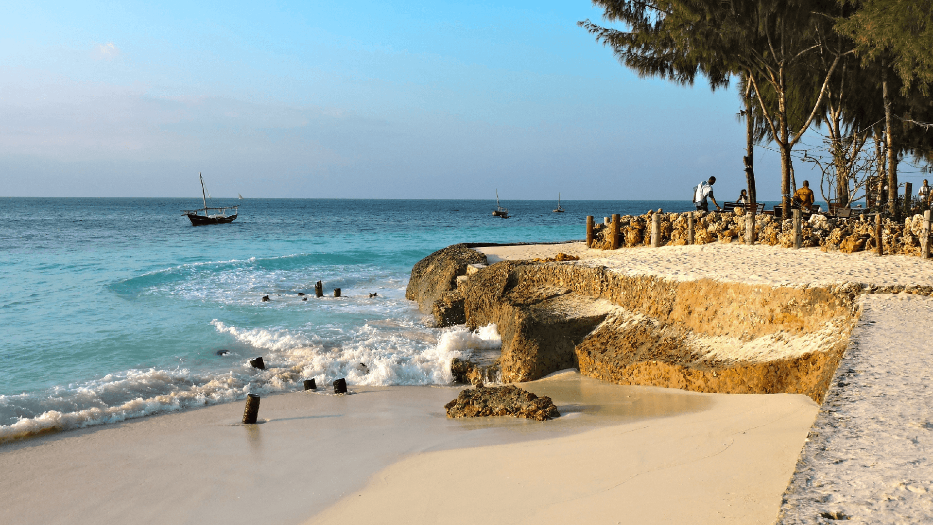 The white sandy beaches of Zanzibar being lapped by clear, turquoise waves with a fishing boat on the horizon captured by Zoe Francis