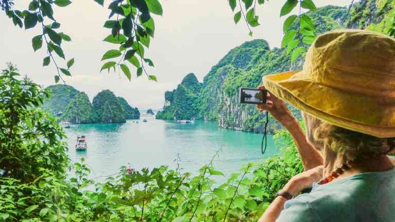 A woman in a yellow hat taking a photo of Halong Bay on a Vietnam tour